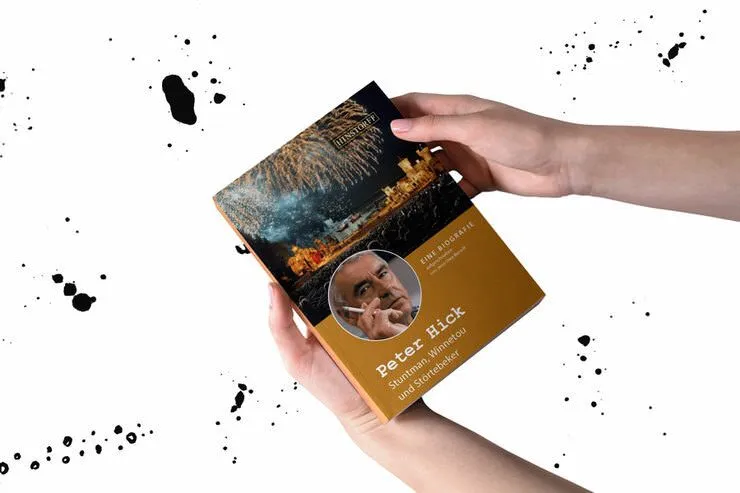 Eine Person hält ein Buch über Peter Hick, umgeben von künstlerischen Spritzern.